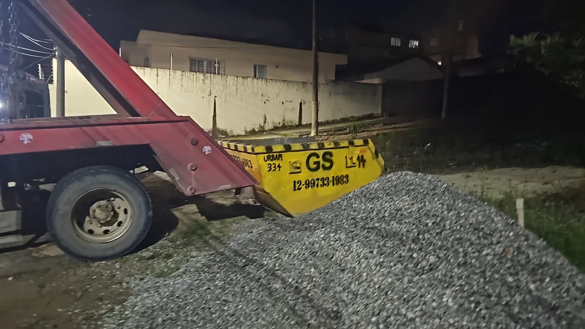 Caminhão poliguindaste vermelho e caçamba amarela da GS durante atendimento à noite