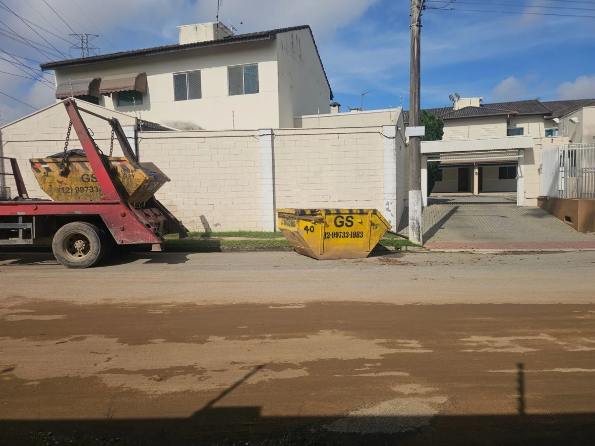 Caminhão poliguindaste vermelho e caçamba amarela da GS diante de imóvel residencial