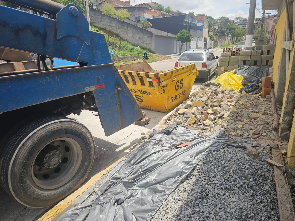 Caçamba amarela da GS junto a caminhão azul e materiais de construção
