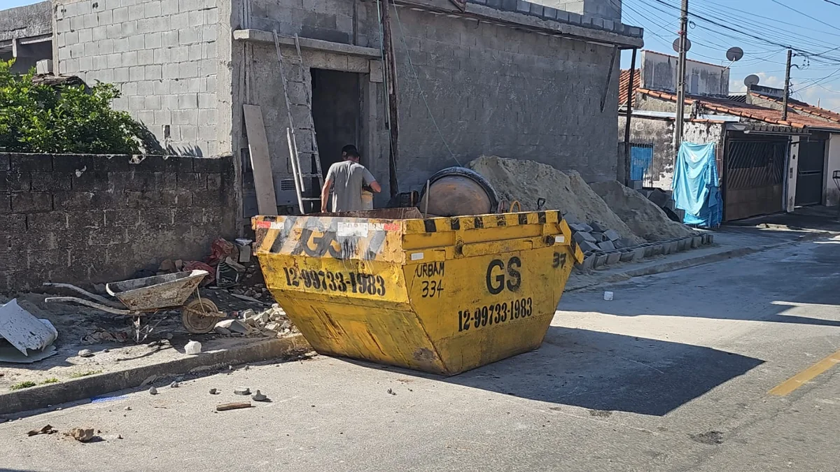 Caçamba amarela da GS com entulho em frente a uma obra residencial