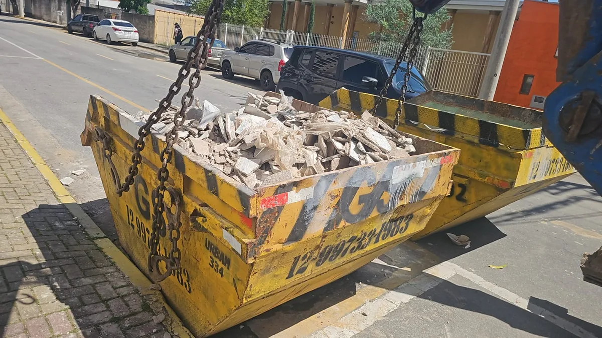 Caçamba da GS com entulho de construção presa às correntes do caminhão