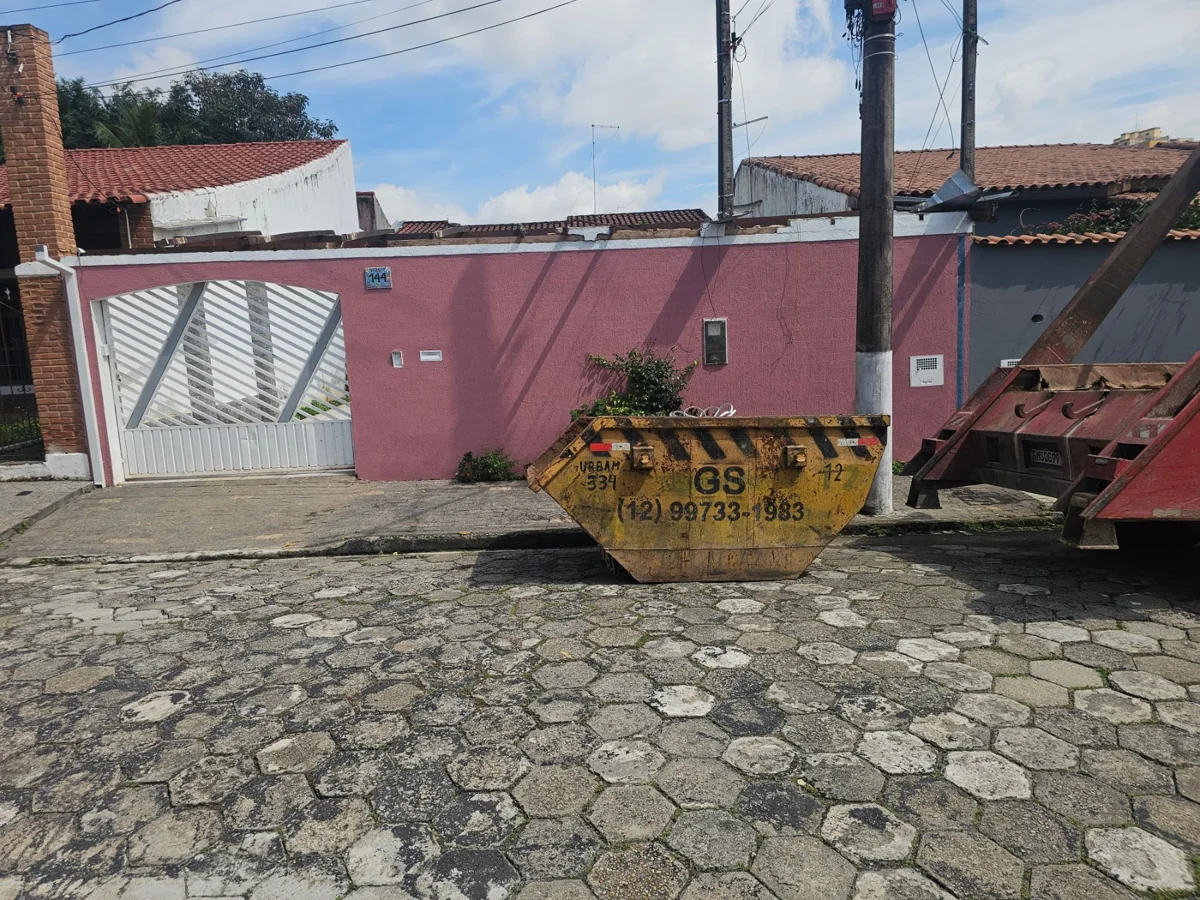 Caçamba amarela da GS junto a caminhão em rua pavimentada com pedras