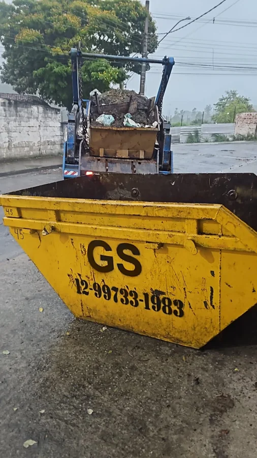 Caçamba amarela da GS em primeiro plano e caminhão poliguindaste ao fundo