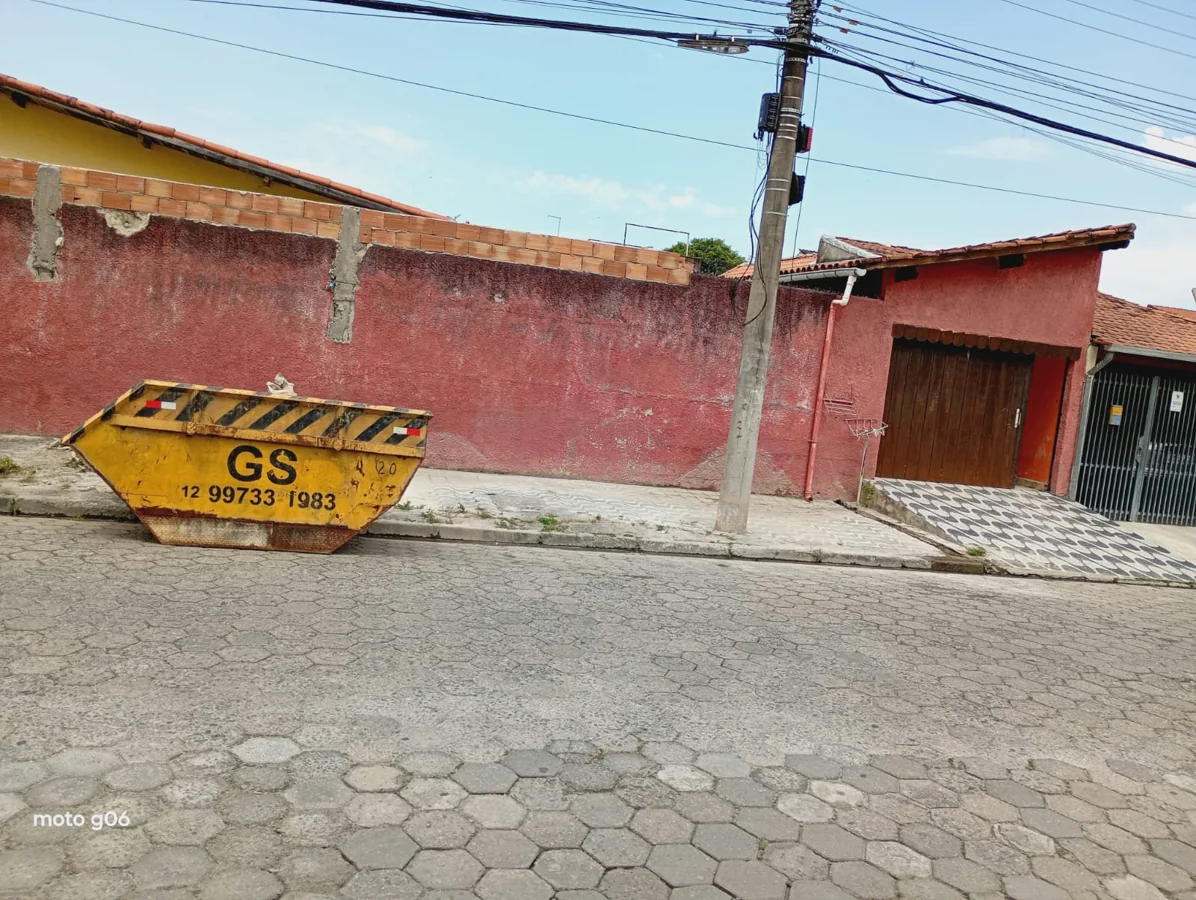Caçamba amarela da GS em rua de pedras diante de muro vermelho