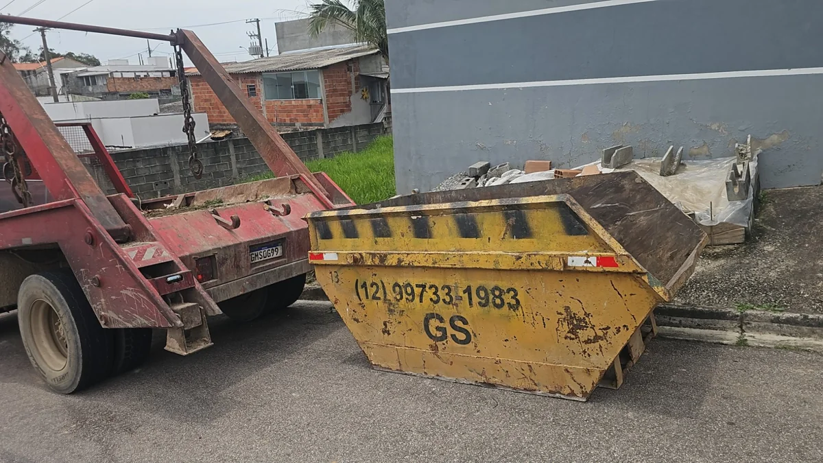 Caçamba amarela da GS com entulho ao lado de caminhão poliguindaste vermelho em rua residencial