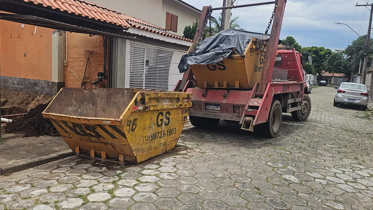 Caminhão vermelho da GS com uma caçamba na carroceria e outra no chão