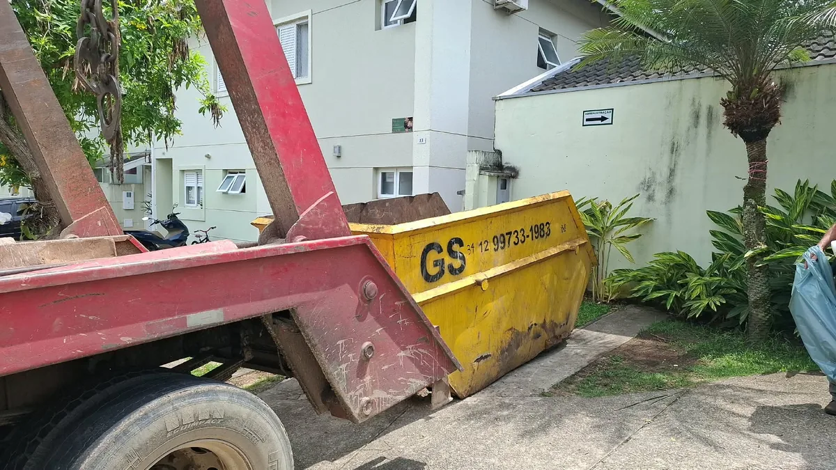 Caçamba amarela da GS ao lado de caminhão poliguindaste e vegetação