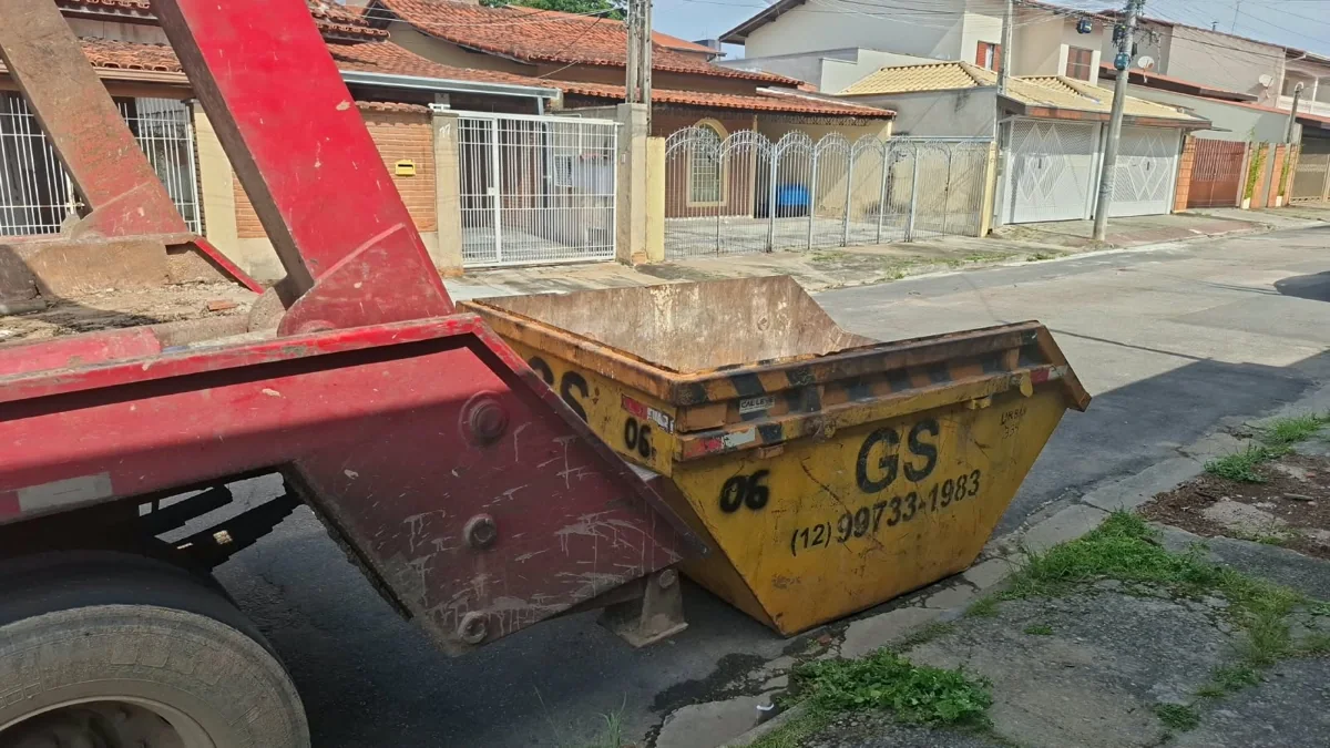 Caminhão poliguindaste vermelho com caçamba amarela da GS em rua residencial